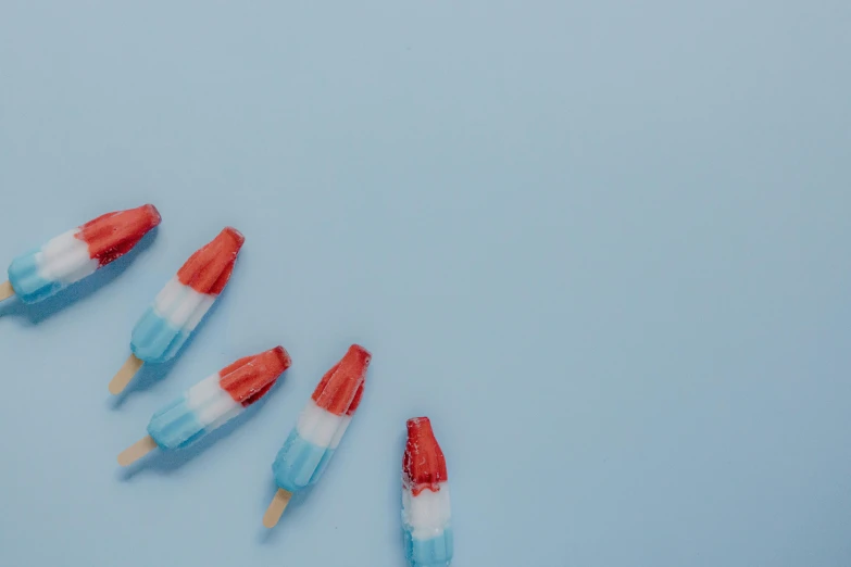 a group of pops sitting on top of a blue surface, trending on pexels, fourth of july, background image, icicle, red and white colors