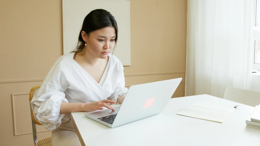 a woman sitting at a table using a laptop computer, inspired by Li Di, pexels, wearing a white blouse, asian descend, 1 2 9 7