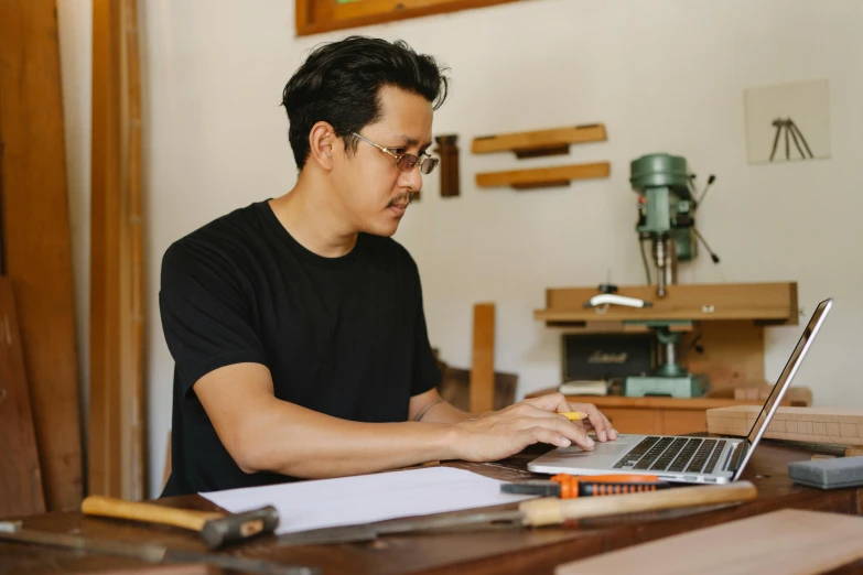 a man sitting at a table using a laptop computer, pexels contest winner, arbeitsrat für kunst, professional woodcarving, asian male, inspect in inventory image, brittney lee