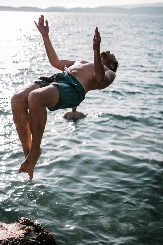 a man jumping off a cliff into the water, hanging upside down, camaraderie, glare on the water, fully functional