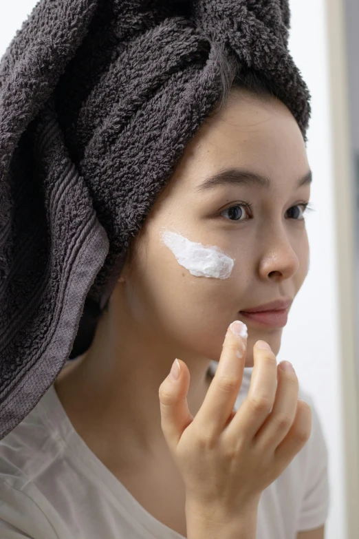 a woman putting cream on her face in front of a mirror, detailed product image, kami, side angle, asian face