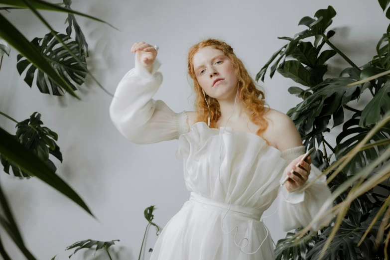 a woman in a white dress standing in front of a plant, an album cover, inspired by Cecil Beaton, trending on pexels, pre-raphaelitism, flowing ginger hair, white sleeves, portrait shot 8 k, sheer fabrics