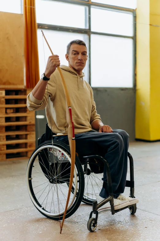 a man in a wheelchair holding a bow and arrow, skin : tjalf sparnaay, grey, big wooden club, brown