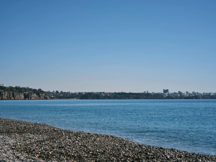 a bench sitting on top of a beach next to a body of water, by Chris Rallis, unsplash, mingei, light blue clear sky, seattle, seen from a distance, ballard