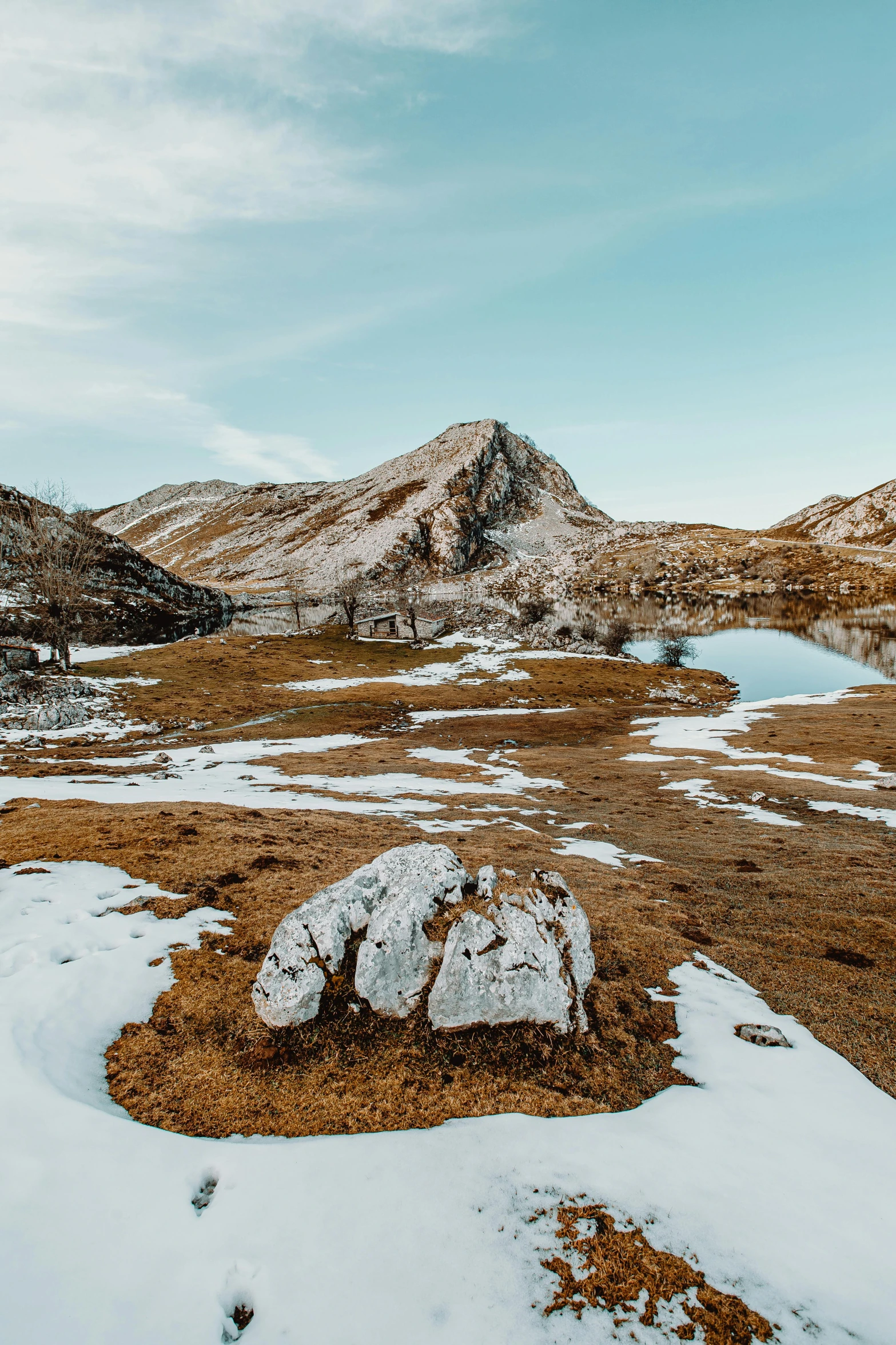 a body of water sitting in the middle of a snow covered field, by Sebastian Spreng, unsplash contest winner, land art, rocky hills, near a small lake, rocky grass field, brown