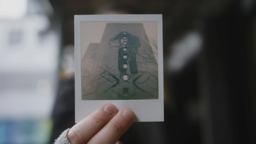 a person holding up a polaroid picture of a building, inspired by Elsa Bleda, pexels contest winner, serial art, symmetrical portrait, transparent holographic being, greenish expired film, low quality footage