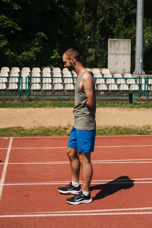 a man standing on top of a tennis court holding a racquet, a portrait, by Attila Meszlenyi, shutterstock, on a racetrack, working out in the field, wearing a tank top and shorts, running shoes