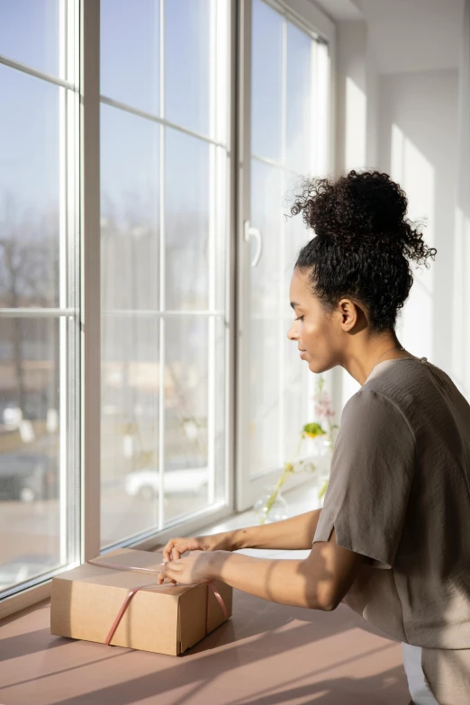 a woman opening a box in front of a window, by Washington Allston, trending on pexels, renaissance, looking off into the distance, black young woman, springtime morning, profile view perspective