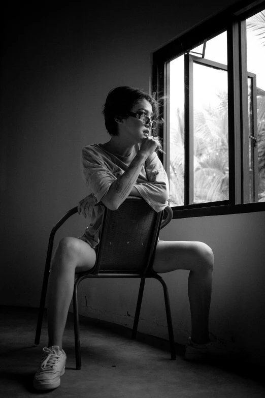 a woman sitting on a chair in front of a window, a black and white photo, inspired by Nan Goldin, flickr, smoking with squat down pose, nivanh chanthara, portrait!!!!!!, casual pose