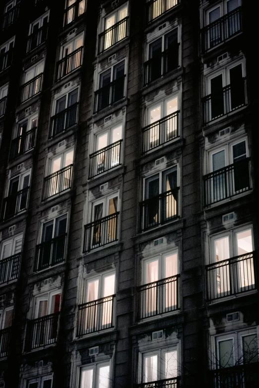 a tall building with lots of windows lit up at night, pexels contest winner, hyperrealism, balconies, analog photo, black windows, ignant