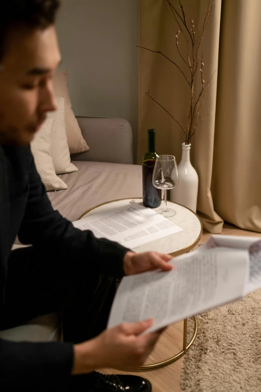 a man sitting on a couch reading a paper, wine, south korean male, official documentation, cozy setting