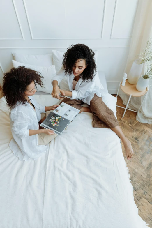 a couple of women sitting on top of a bed, brown and white color scheme, reading a book, flat lay, multiple stories