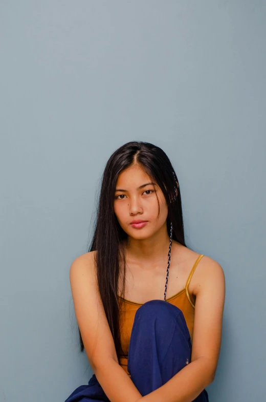 a woman sitting on the ground with her legs crossed, inspired by helen huang, unsplash, minimalism, long thin black hair, blue backdrop, 🤤 girl portrait, wearing a camisole