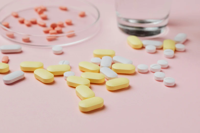 pills and a glass of water on a pink surface, inspired by Évariste Vital Luminais, antipodeans, white and yellow scheme, up-close, on a table, half turned around