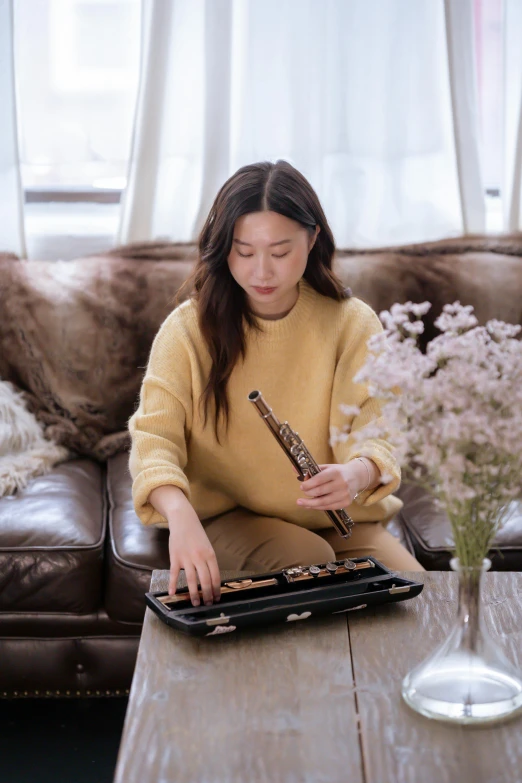 a woman sitting on a couch playing a musical instrument, an album cover, inspired by Song Xu, trending on pexels, young girl playing flute, 🚿🗝📝