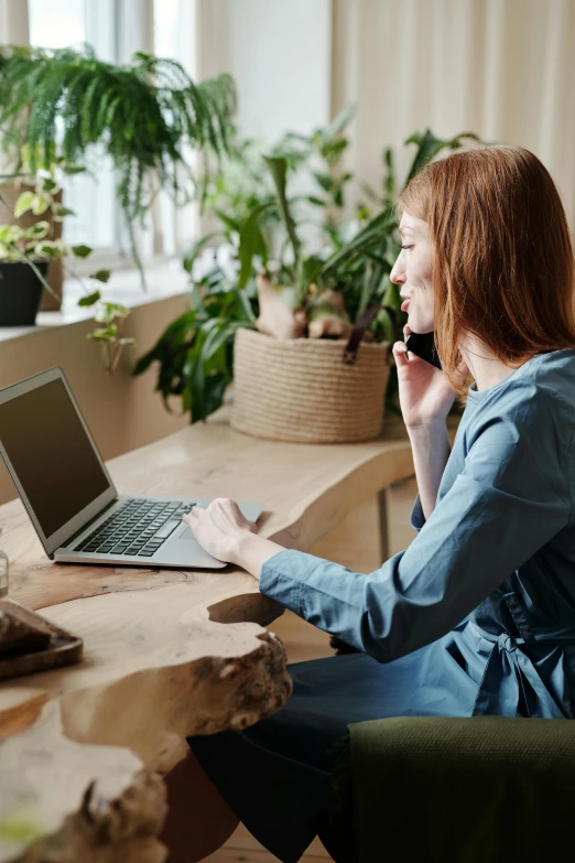 a woman sitting at a table using a laptop computer, trending on pexels, renaissance, girl making a phone call, a redheaded young woman, sustainable materials, facing sideways