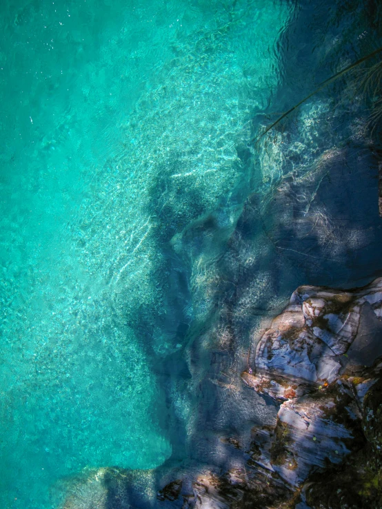 a body of water surrounded by rocks and trees, a screenshot, by Jacob Toorenvliet, unsplash contest winner, crystal clear blue water, camera looking down upon, shimmering iridescent water, today\'s featured photograph 4k