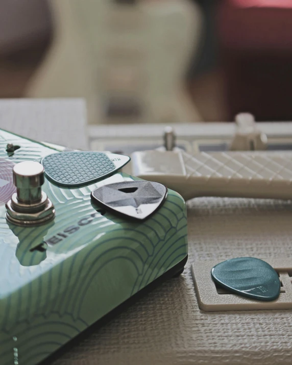 a guitar sitting on top of a table next to a guitar pick, dials, teal, multi - coloured, rectangle