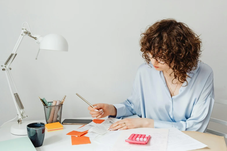 a woman sitting at a desk using a cell phone, by Julia Pishtar, trending on pexels, holding pencil, 9 9 designs, papers on table, slightly minimal