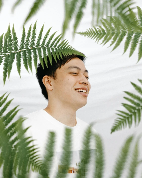 a man standing in front of a bunch of green leaves, an album cover, inspired by Liang Kai, pexels contest winner, sumatraism, happy expression, fern, profile image, grinning lasciviously