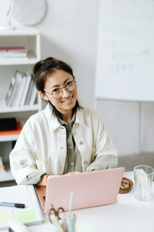 a woman sitting at a table with a laptop, cute slightly nerdy smile, standing in class, gemma chen, plain background