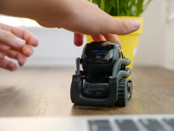 a small toy car sitting on top of a wooden table, a picture, les automatistes, the microchip, bending down slightly, back of hand on the table, crawling towards the camera