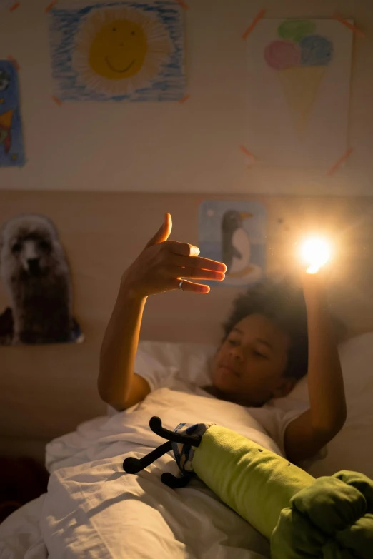 a person laying in a bed with a flashlight in their hand, light and space, light over boy, forming a burning hand spell, ignant, concerned