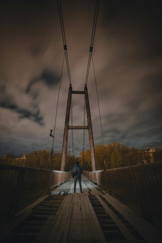 a person standing on a bridge at night, by Sebastian Spreng, ominous skies, connected with hanging bridge!!, distant full body view, dramatic light 8 k