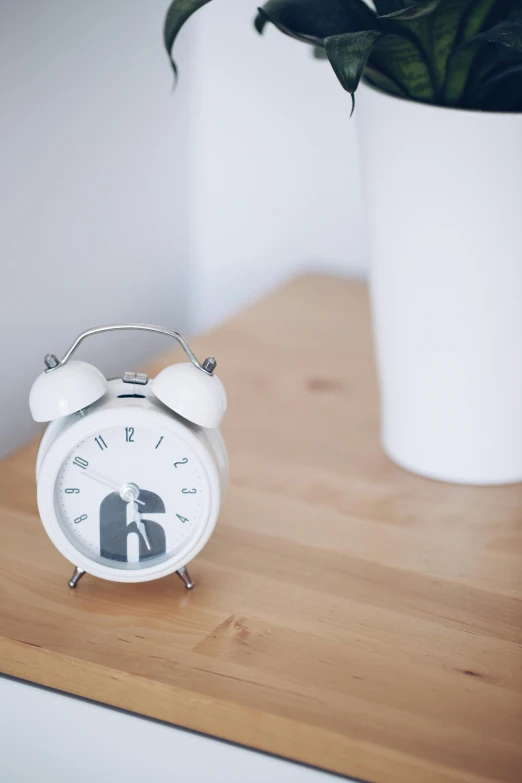 a white clock sitting on top of a wooden table, detailed product image, holding a bell, high res photograph, sleepy