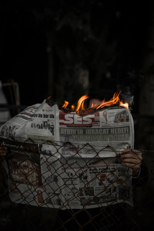 a person holding a newspaper in front of a fire, by Ibrahim Kodra, pexels contest winner, human sacrifice, turkey, cardboard, cover shot