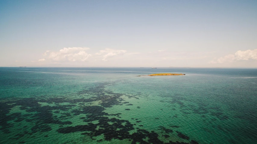 a small island in the middle of the ocean, by Peter Churcher, unsplash, cyan and green, sydney hanson, islands on horizon, slightly tanned