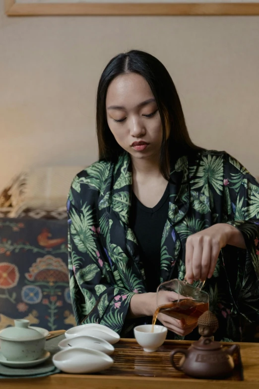 a woman sitting at a table pouring tea into a cup, a portrait, inspired by Pan Yuliang, trending on unsplash, wearing a fancy jacket, gif, with hawaiian shirt, medium format