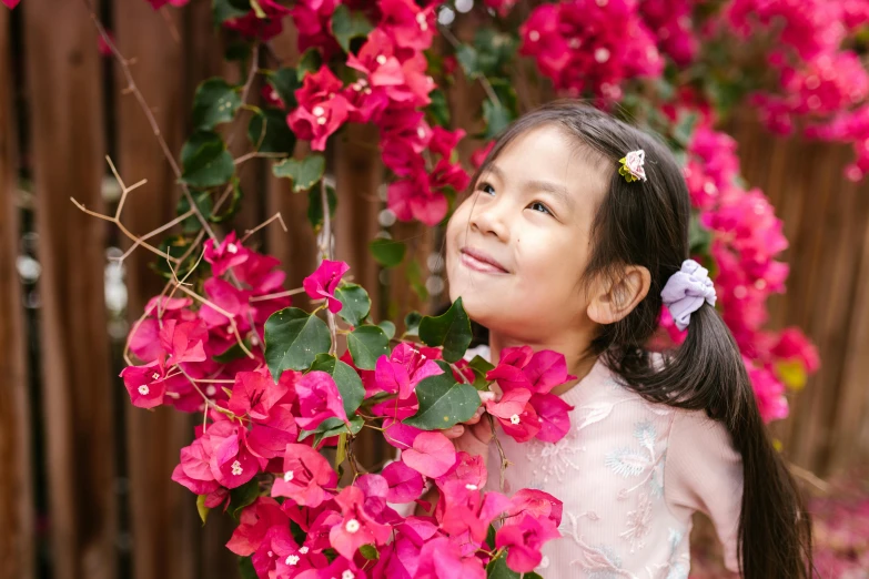 a little girl standing in front of a bunch of flowers, inspired by Cui Bai, pexels contest winner, hurufiyya, bougainvillea, looking happy, chinese heritage, with ivy