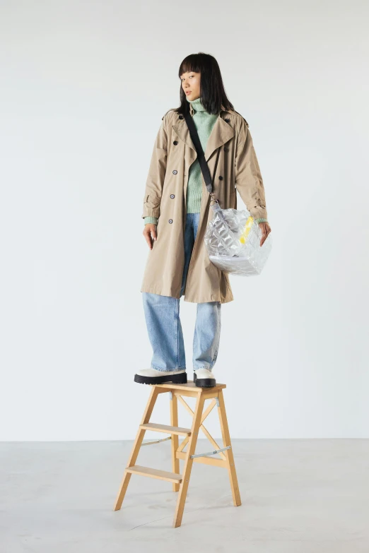 a woman standing on a stool holding a bag, light brown trenchcoat, けもの, trending on r/streetwear, h 576