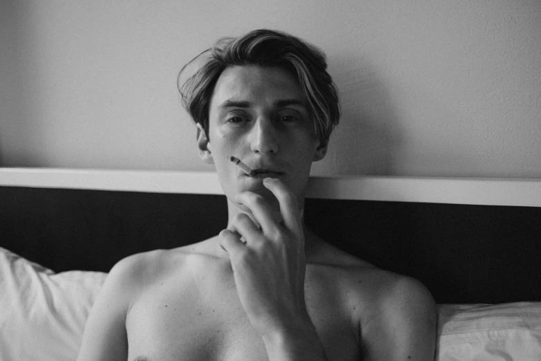 a shirtless man sitting on top of a bed, by Emma Andijewska, aestheticism, thick jawline, cigarette in his mouth, long swept back blond hair, portrait featured on unsplash