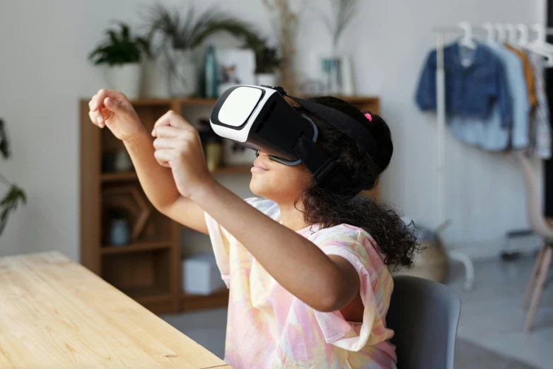 a little girl sitting at a table using a virtual reality headset, a picture, inspired by Jean Tabaud, unsplash, interactive art, black, over-shoulder shot, medium-shot, wearing 3 d glasses