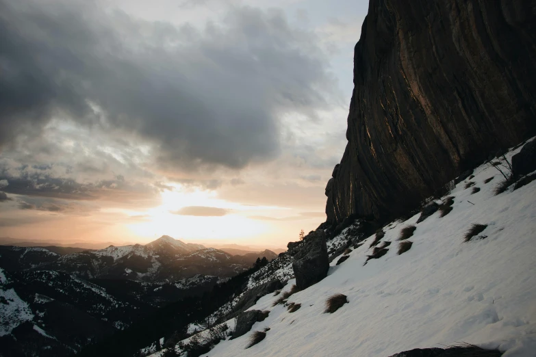 a man riding skis down a snow covered slope, a picture, unsplash contest winner, cliff side at dusk, 4 k hd wallpapear, rocky cliff, sunset with cloudy skies