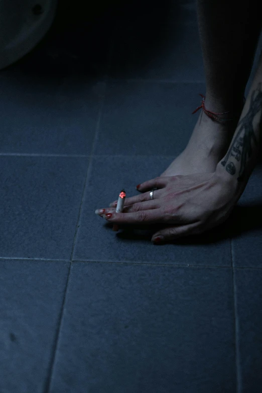 a person sitting on the floor with a cigarette in their hand, a tattoo, inspired by Elsa Bleda, lights off, drugs, **cinematic, low iso