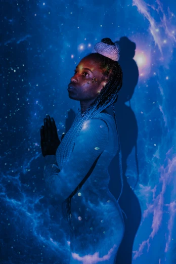 a man standing in front of a blue background, an album cover, trending on pexels, afrofuturism, powerful woman sitting in space, glowing holy aura, standing with a black background, in a space starry