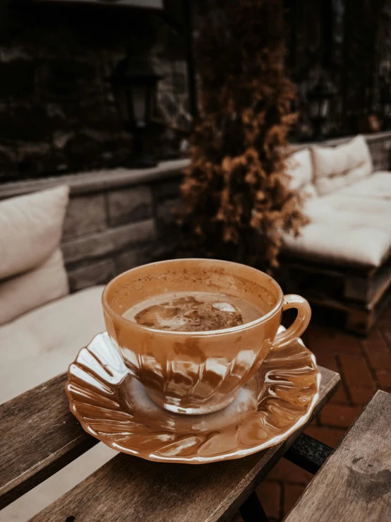 a cup of coffee sitting on top of a wooden table, beige and gold tones, thumbnail, heavy winter aesthetics, rustic setting