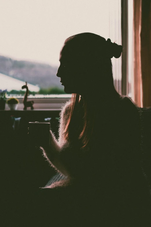 a silhouette of a woman sitting in front of a window, inspired by Elsa Bleda, pexels contest winner, drinking coffee, woman with cat ears, grainy quality, low quality photo