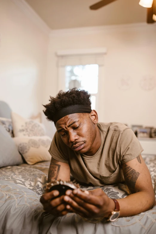 a man laying on a bed holding a cell phone, trending on pexels, renaissance, portrait of depressed teen, man is with black skin, playing games, androgynous male