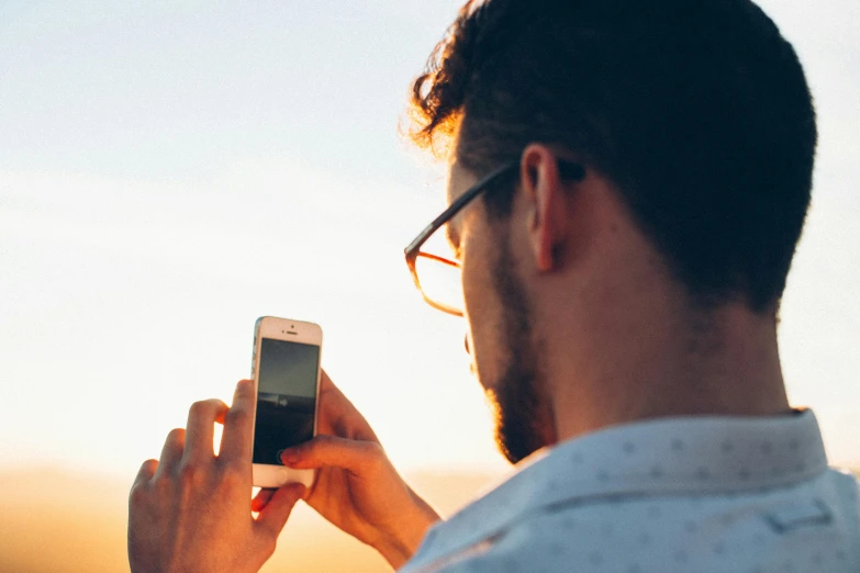 a close up of a person holding a cell phone, a picture, trending on pexels, happening, man with glasses, gazing off into the horizon, sunfaded, avatar image