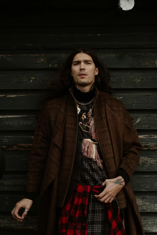 a man standing in front of a wooden wall, an album cover, trending on pexels, renaissance, hozier, metal garments, jean deville, brown cloak