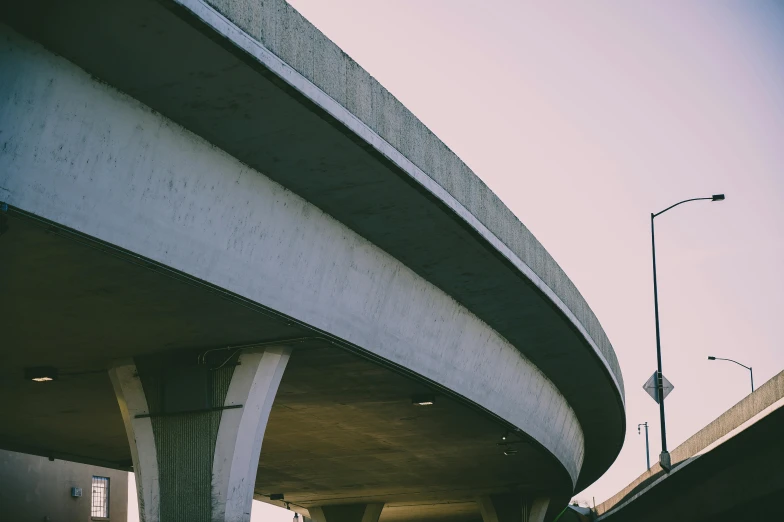 a man riding a skateboard up the side of a ramp, unsplash, brutalism, overpass, intersection, 90's photo, rounded architecture