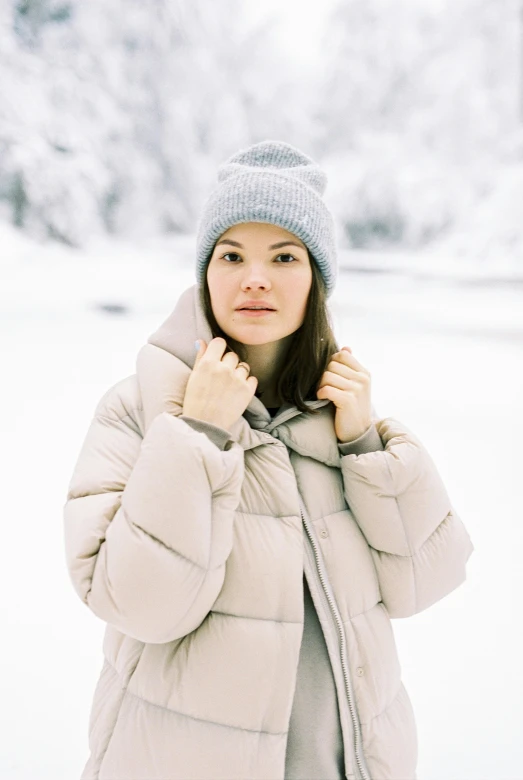 a woman standing in the snow wearing a jacket and hat, inspired by Louisa Matthíasdóttir, trending on pexels, light grey, brunette, puffer jacket, pale blue