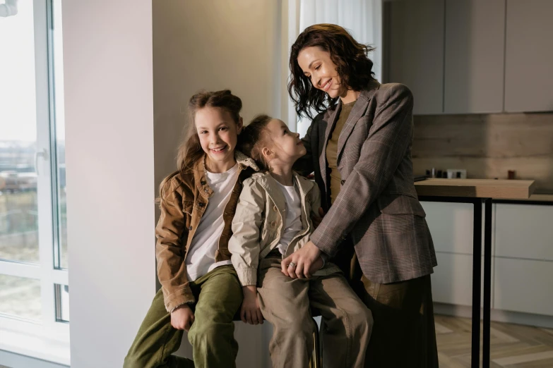 a woman and two children sitting on a stool, a picture, pexels, brown jacket, high quality photos, high quality picture, trending on