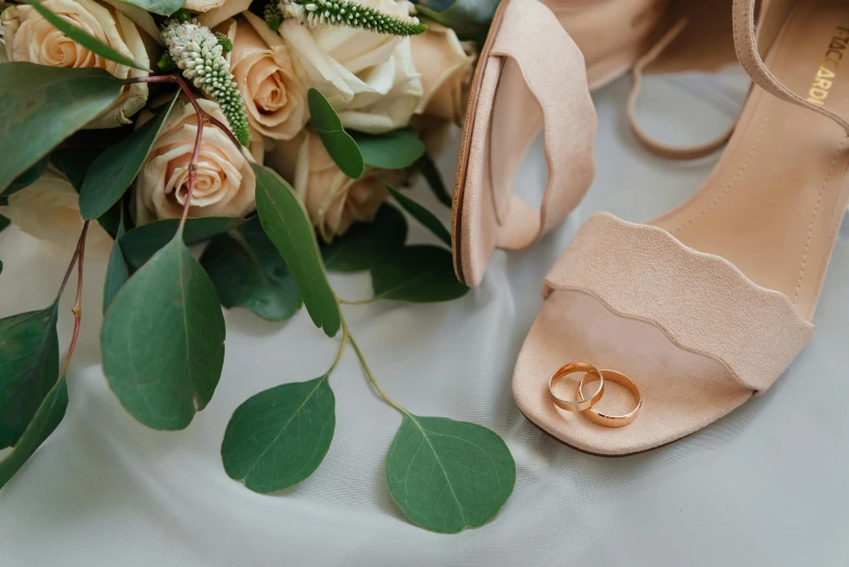 a pair of shoes sitting next to a bouquet of flowers, gold rings, in shades of peach, neutral colours, thumbnail