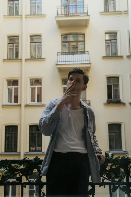 a man standing on a balcony smoking a cigarette, pexels contest winner, young handsome pale roma, warsaw, profile image, wearing a light shirt
