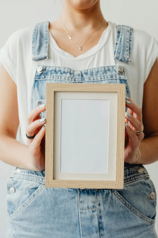 a woman holding a picture frame in her hands, poster art, pexels contest winner, square pictureframes, wearing overalls, craft, blonde crea